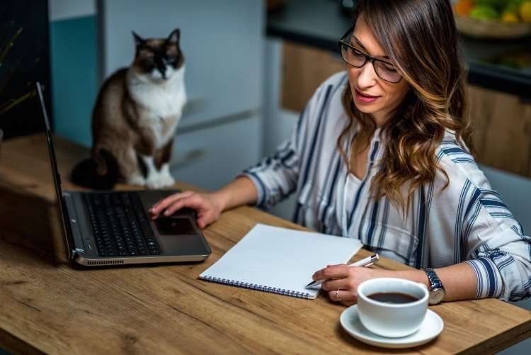 young-woman-drinking-coffee-and-working-at-home-P5QBM6A-750x501